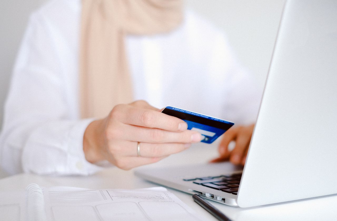 Close-up of a person holding a credit card while using a laptop for online shopping.