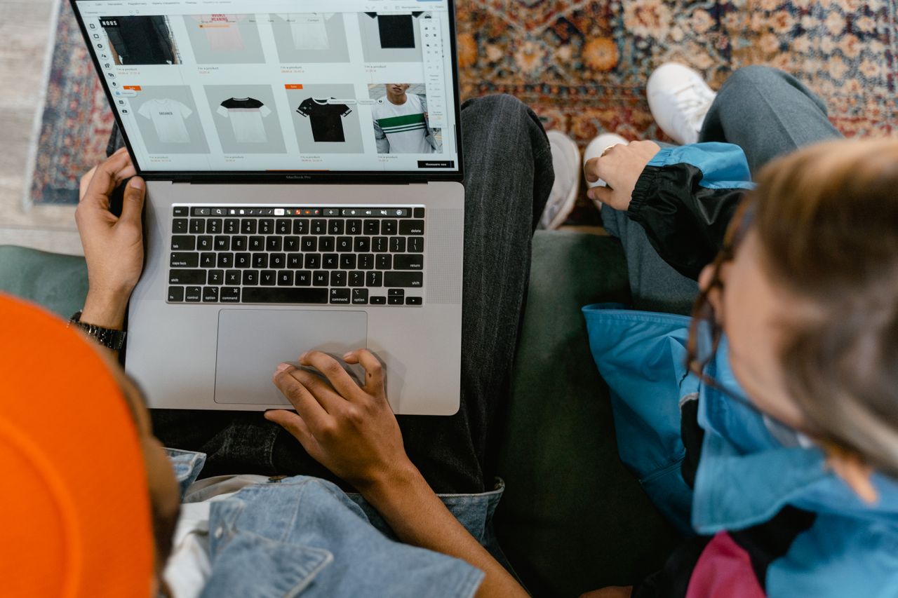 Two people browsing online clothing store on a laptop from above.